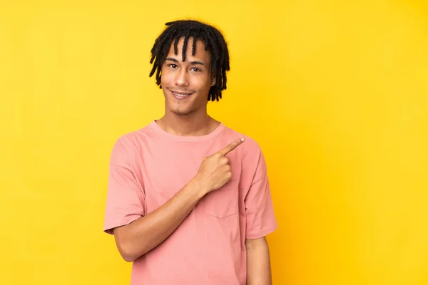製品を提示するために側面を指す黄色の背景に隔離された若いアフリカ系アメリカ人男性 — ストック写真