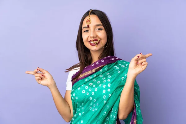年轻的印度妇女被紫色背景隔离 手指指向侧边 很快乐 — 图库照片
