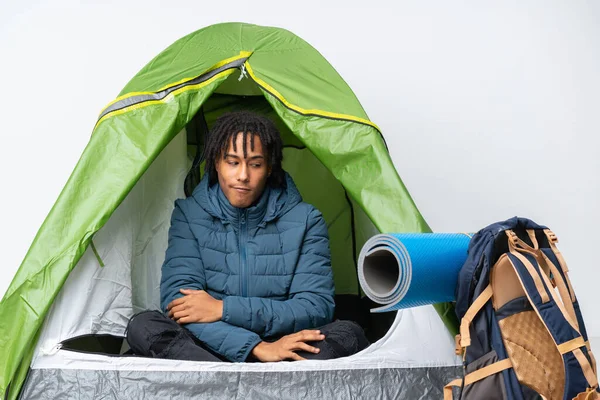Young african american man inside a camping green tent making doubts gesture looking side