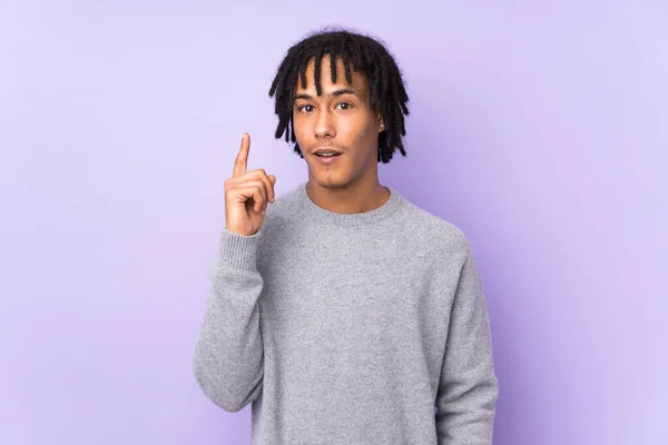 アフリカ系アメリカ人の若い男が紫色の背景に指を指差すアイデアを考え — ストック写真