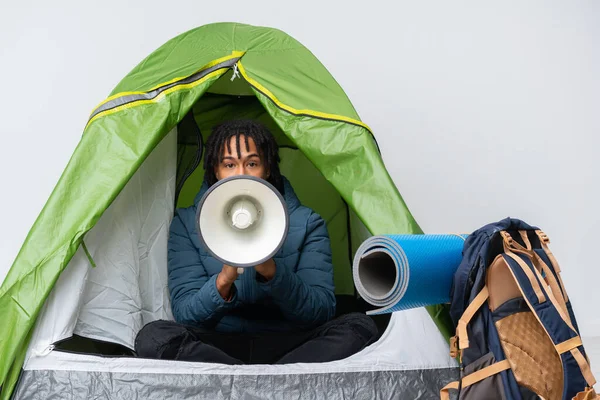 Young african american man inside a camping green tent shouting through a megaphone