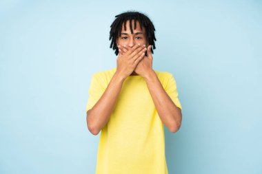 Genç Afro-Amerikalı adam mavi arka planda izole edilmiş ağızlarını elleriyle kapatıyor.