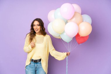 Mor arka planda zaferi kutlayan balonları yakalayan genç bir kadın.