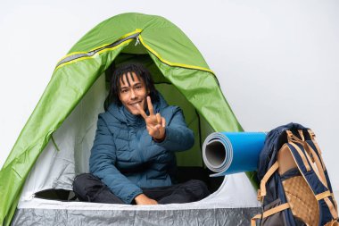 Genç Afro-Amerikan bir adam kamp yeşil çadırında gülümsüyor ve zafer işareti gösteriyor.