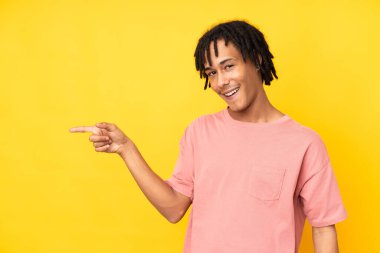 Sarı arka planda izole edilmiş genç bir Afrikalı Amerikalı parmak göstererek bir ürün sunuyor.