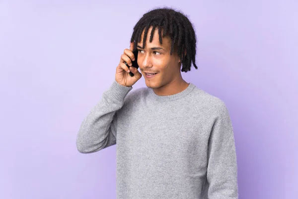 紫色の背景に隔離された若いアフリカ系アメリカ人の男誰かと携帯電話との会話を続ける — ストック写真