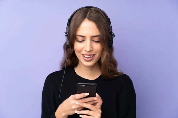 Mujer Joven Sobre Fondo Púrpura Aislado Escuchando Música Mirando Móvil —  Fotos de Stock