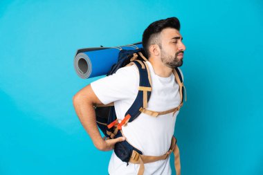 Genç dağcı, izole edilmiş mavi arka planda çabaladığı için sırt ağrısı çekiyor.
