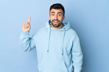 İzole edilmiş mavi arka planı olan beyaz bir adam harika bir fikre işaret ediyor.