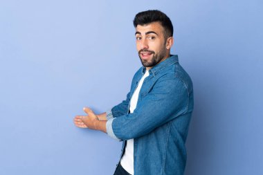 İzole edilmiş mavi arka planda beyaz bir adam. Davet etmek için ellerini yana uzatıyor.