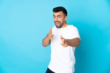 İzole edilmiş mavi arka plan üzerinde beyaz bir adam ön tarafı işaret ediyor ve gülümsüyor.