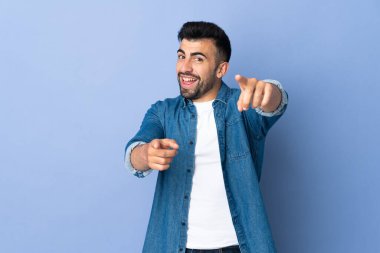 İzole edilmiş mavi arka plan üzerinde beyaz bir adam mutlu bir ifadeyle önü işaret ediyor.