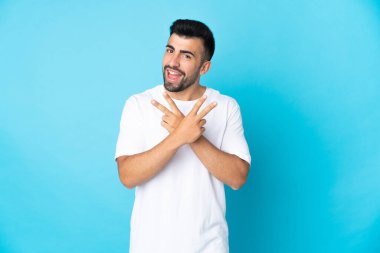 İzole edilmiş mavi arka plan üzerinde gülümseyen ve zafer işareti gösteren beyaz bir adam.