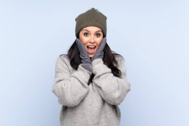 Kışlık şapkalı genç Kolombiyalı kız izole edilmiş mavi bir arka plan ve şaşırtıcı yüz ifadesi var.