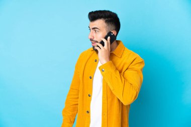 İzole edilmiş mavi arka planı olan beyaz bir adam cep telefonuyla sohbet ediyor.