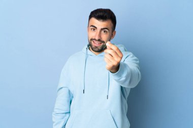 İzole edilmiş mavi arka planda beyaz bir adam para hareketi yapıyor.