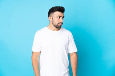 İzole edilmiş mavi arka planda beyaz bir adam yan tarafa bakıyor.