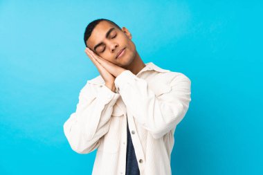 Genç Afro-Amerikalı bir adam mavi arka plan üzerinde uyku jesti yapıyor.