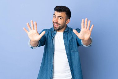 İzole edilmiş mavi arka planda beyaz adam parmaklarıyla 10 'a kadar sayıyor.