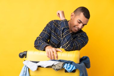 Bir bavul dolusu elbisesi olan, izole edilmiş sarı arka planı olan bir gezgin.