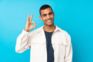 Genç Afro-Amerikalı adam izole edilmiş mavi arka planda parmaklarıyla işaret veriyor.