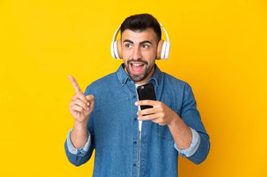 İzole edilmiş sarı arka plan üzerinde beyaz bir adam cep telefonuyla müzik dinliyor ve şarkı söylüyor.