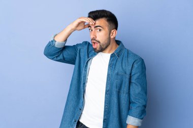 İzole edilmiş mavi arka plan üzerinde beyaz bir adam yan tarafa bakarken sürpriz jest yapıyor.