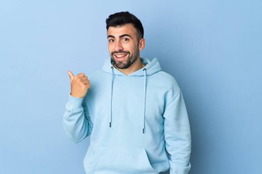 İzole edilmiş mavi arka planda beyaz bir adam bir ürünü sunmak için kenarı işaret ediyor.