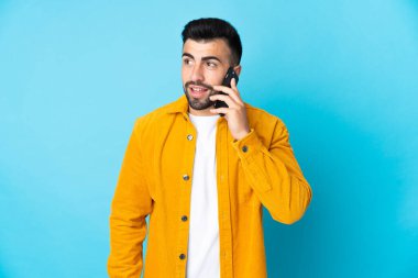 İzole edilmiş mavi arka planı olan beyaz bir adam cep telefonuyla sohbet ediyor.