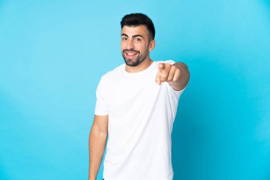 İzole edilmiş mavi arka plan üzerinde beyaz bir adam mutlu bir ifadeyle önü işaret ediyor.