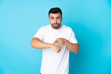 İzole edilmiş mavi arka planda beyaz bir adam geç kalma jesti yapıyor.