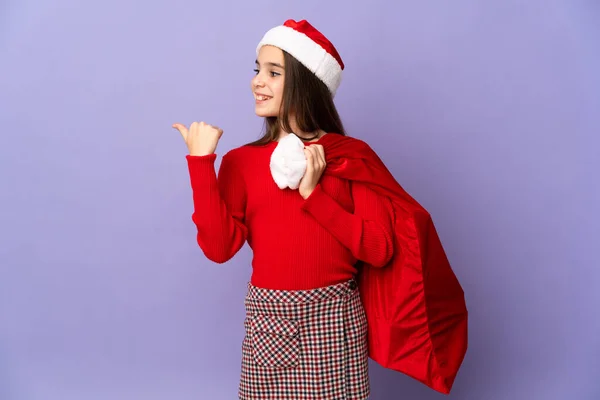 Kleines Mädchen Mit Hut Und Weihnachtstasche Isoliert Auf Lila Hintergrund — Stockfoto