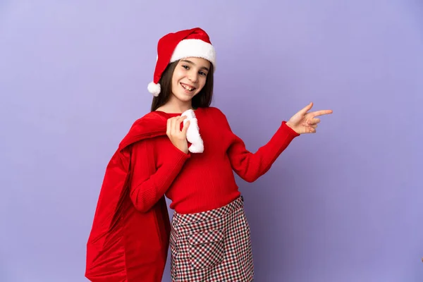 Little Girl Hat Christmas Sack Isolated Purple Background Pointing Finger — Stock Photo, Image