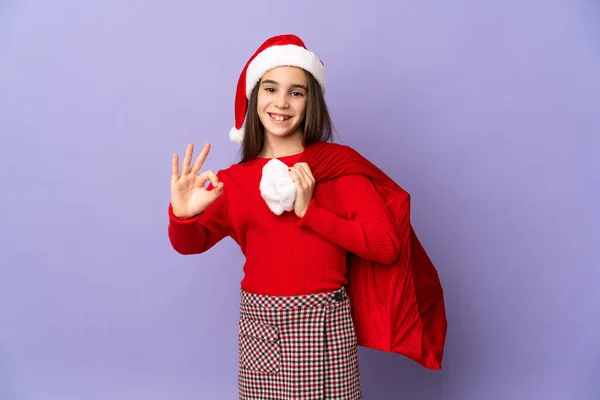 Kleines Mädchen Mit Hut Und Weihnachtssack Isoliert Auf Lila Hintergrund — Stockfoto