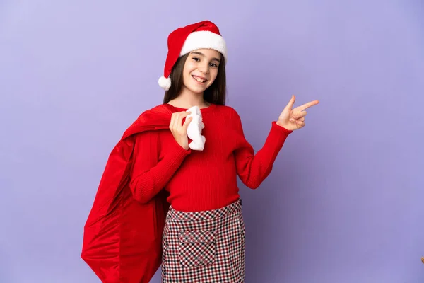 Little Girl Hat Christmas Sack Isolated Purple Background Pointing Finger — Stock Photo, Image