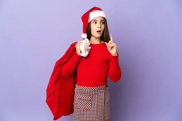 Kleines Mädchen Mit Hut Und Weihnachtssack Isoliert Auf Lila Hintergrund — Stockfoto