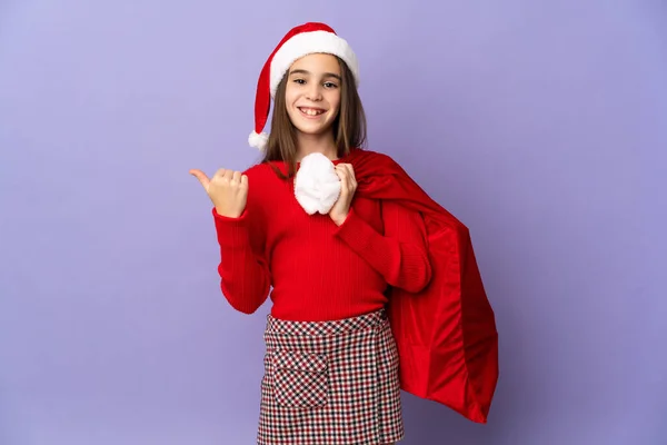 Kleines Mädchen Mit Hut Und Weihnachtstasche Isoliert Auf Lila Hintergrund — Stockfoto
