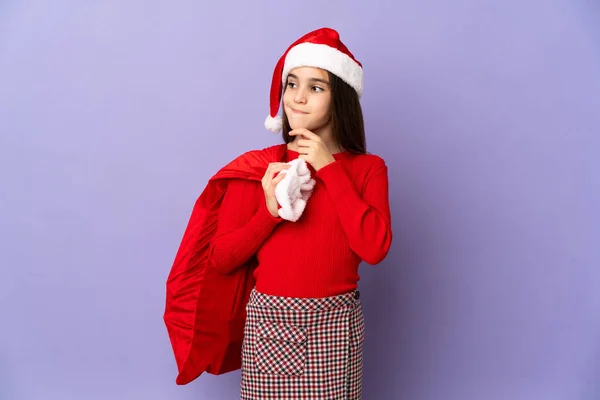 Kleines Mädchen Mit Hut Und Weihnachtssack Isoliert Auf Lila Hintergrund — Stockfoto