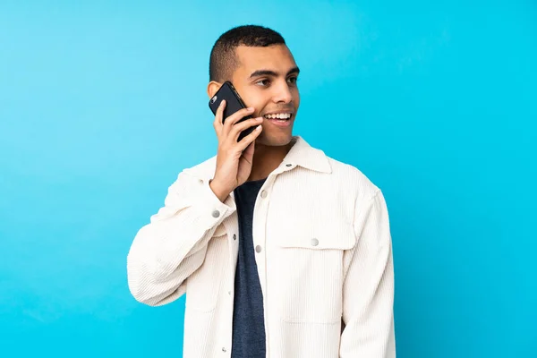 Mladý Afroameričan Přes Izolované Modré Pozadí Udržet Rozhovor Mobilním Telefonem — Stock fotografie