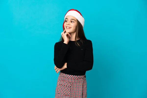 Kleines Mädchen Mit Weihnachtsmütze Isoliert Auf Blauem Hintergrund Beim Nachdenken — Stockfoto
