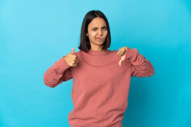 Mavi arka planda izole edilmiş genç Latin kadın iyiye-kötüye işaret yapıyor. Evet ya da hayır arasında kararsız