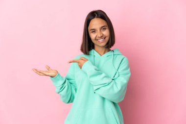 Pembe arka planda izole edilmiş genç Latin bir kadın bir ilan vermek için avucunun içinde hayali bir alan tutuyor.