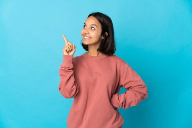 Mavi arka planda izole edilmiş genç Latin kadın harika bir fikre işaret ediyor.