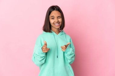 Pembe arka planda izole edilmiş genç Latin kadın ön tarafı işaret ediyor ve gülümsüyor.