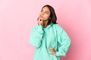 Pembe arka planda izole edilmiş genç Latin kadın yukarı bakarken şüpheleri var.