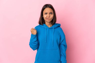 Pembe arka planda, mutsuz bir ifadeyle izole edilmiş genç Latin kadın.