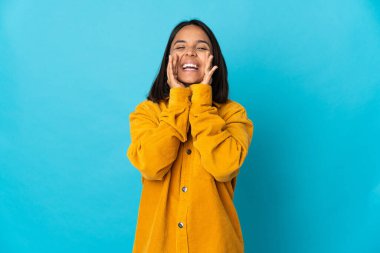 Genç Latin kadın mavi arka planda izole edilmiş bağırıyor ve bir şey duyuruyor.