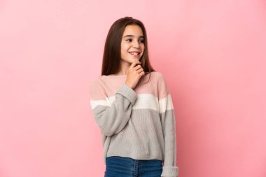 Pembe arka planda soyutlanmış küçük bir kız yan bakıyor ve gülümsüyor.