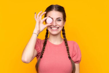 Renkli Fransız badem kurabiyeleriyle izole edilmiş sarı arka planı olan genç bir kadın.