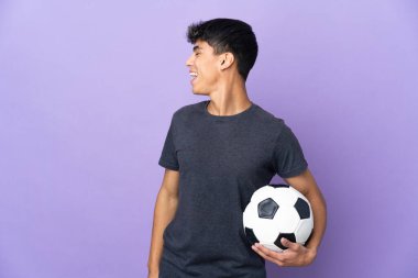Young football player man over isolated purple background laughing in lateral position